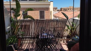 A balcony with a wicker chair, potted plants, and a view of neighboring buildings.