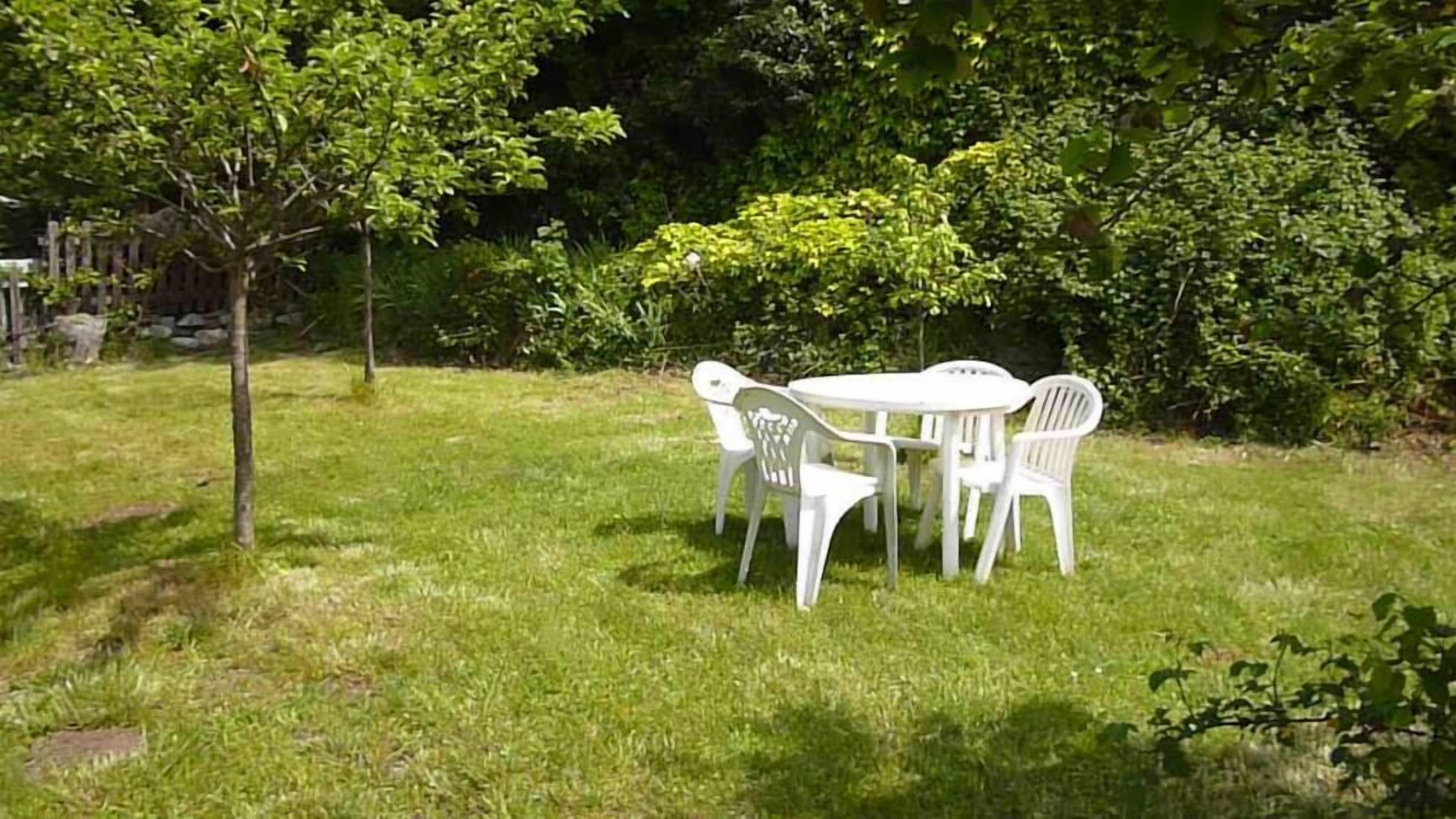 A grassy outdoor area with a round table and four white plastic chairs.