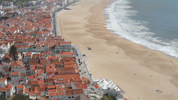 Una ciudad costera con una extensa playa de arena y una zona densamente poblada de edificios con tejas rojas.