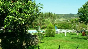 Un exuberante jardín con piscina, sillas reclinables blancas y un muro de piedra.