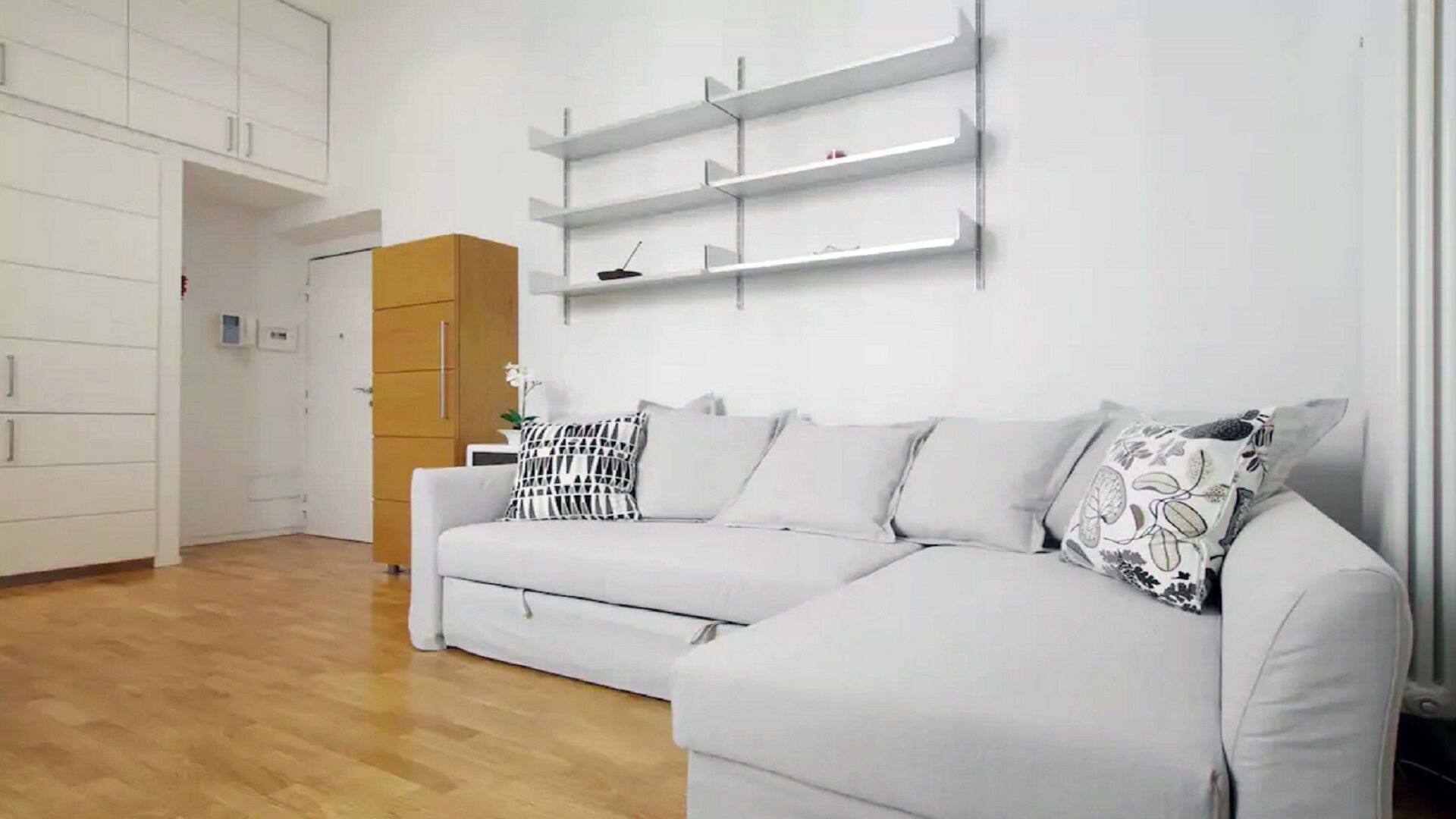 A modern living room with a grey sofa, white walls, and wooden flooring.