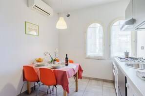 A dining area with a table set for four, chairs, a hanging light fixture, and a window with a view.