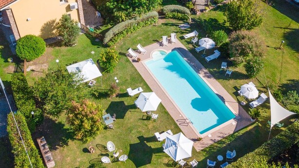 Vista aérea de una piscina rectangular rodeada de césped, con múltiples sillas de descanso y sombrillas.