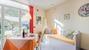 A bright room with a dining table set for two, a sofa with cushions, and a large window with curtains. - Apartment "Yellow", with pool, Villa Gabriella (Lucca)