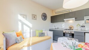 A modern apartment with a living area featuring a sofa with cushions, a dining table with a vase of flowers, and a kitchen with grey cabinets and a stove. - Apartment "Yellow", with pool, Villa Gabriella (Lucca)