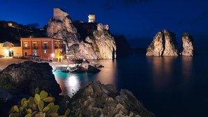 Un edificio costero con una formación rocosa destacada al fondo, una vista despejada del mar y un área de entrada bien iluminada.