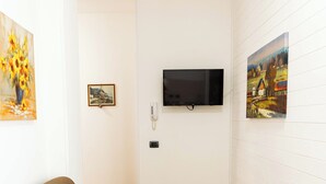 Una habitación con sofá, una mesa de comedor con sillas, un televisor de pantalla plana montado en la pared y suelo de baldosas.