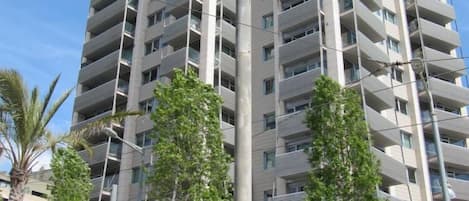 Um edifício residencial alto com várias varandas, um sinal de travessia de pedestres e uma rua com palmeiras.