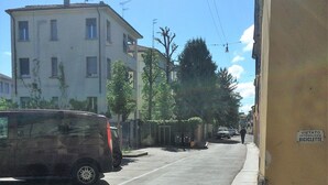 Una strada con auto parcheggiate, edifici e un segnale che indica l'ingresso per biciclette.