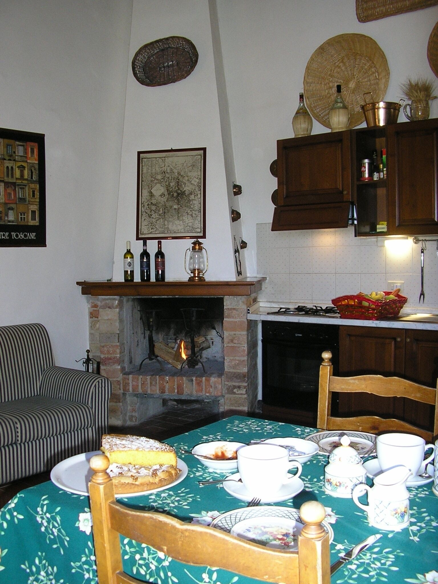 Eine gemütliche Küche mit Kamin aus Ziegelsteinen, Holzschränken und einem für Tee gedecktem Esstisch.