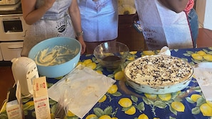 Three people in a kitchen with a table set for a meal, a cake, and various kitchen appliances.