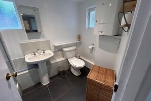 Un bany petit i funcional amb un lavabo blanc, vàter i una petita cistella de vimet.