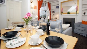 A dining area with a table set for two, a bottle of wine, and a vase with flowers. - Brilliant Fulham Experience - Garden (Private) Apartment (London)