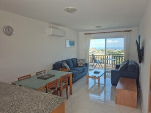 A living room with a dining area, a sofa, a TV, and a balcony with a view.