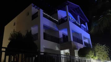 A multi-story building with balconies, a gated entrance, and a well-lit facade at night.