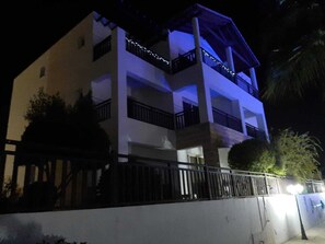 A multi-story building with balconies, a gated entrance, and a well-lit facade at night.