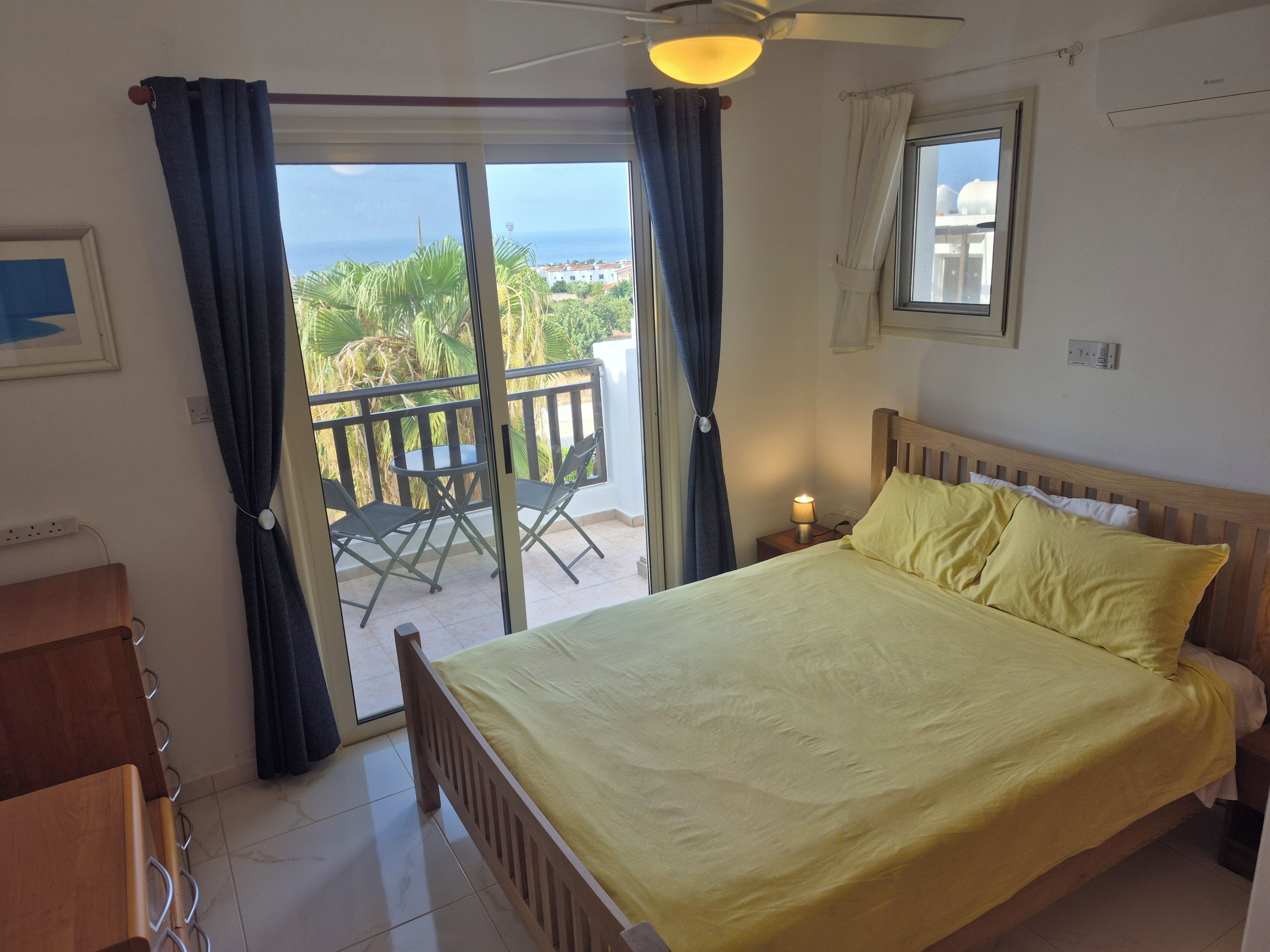 Un dormitorio con cama, mesita de noche, lámpara, ventana y vista al mar.