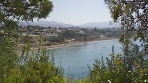 Vista costera con casas a lo largo de la playa, cielo despejado y montañas en la distancia.