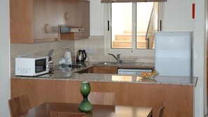 Cocina compacta con armarios de madera, microondas, hervidor y refrigerador.