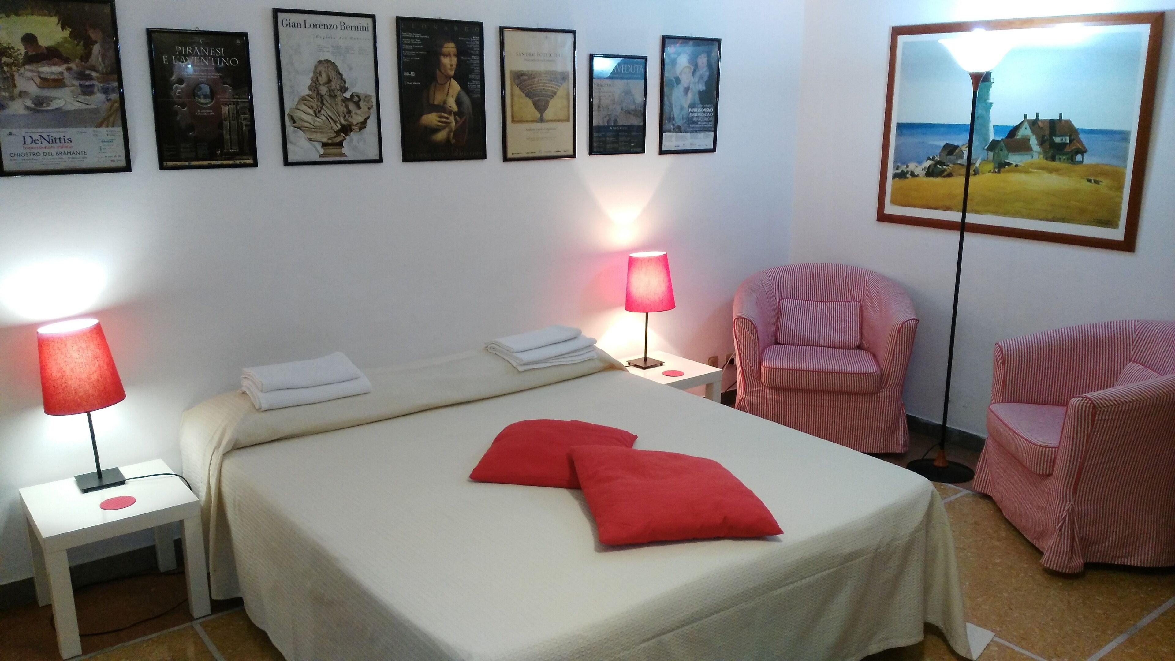 A hotel room with a bed, two chairs, a nightstand, and a wall with framed artwork.