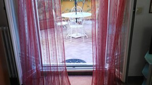 A view through a glass door with red curtains, leading to an outdoor patio with a table and chairs.