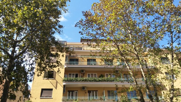 A multi-story building with balconies, air conditioning units, and a clear blue sky.