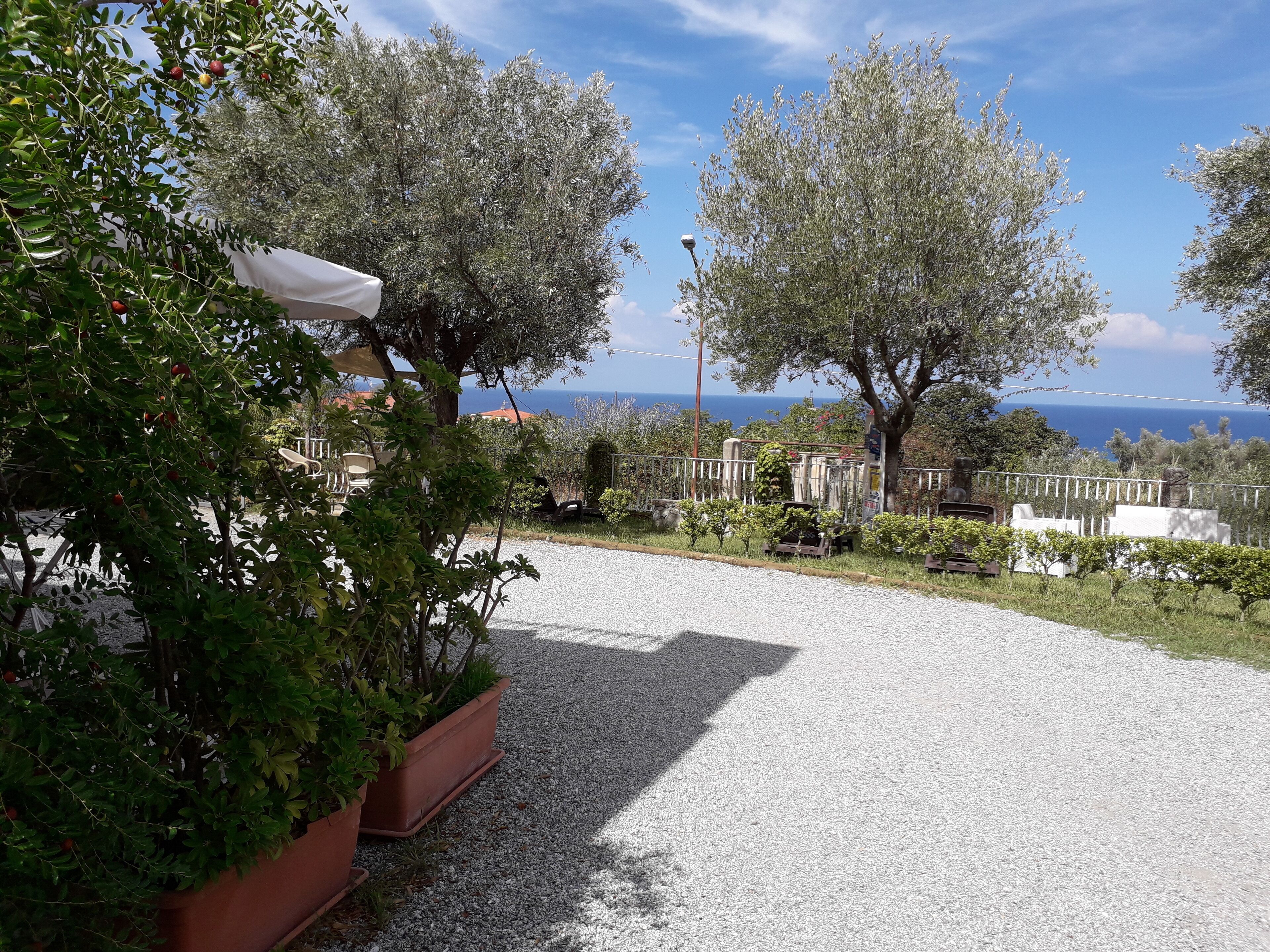 Eine Schotterterrasse mit Kübelpflanzen, einem weißen Zelt und Blick aufs Meer.