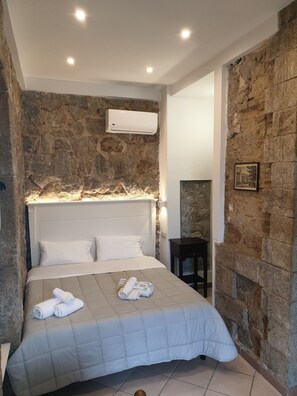 A modern bedroom with a stone wall, a white bed, and a nightstand. - Studio in villa with sea view (Tropea)
