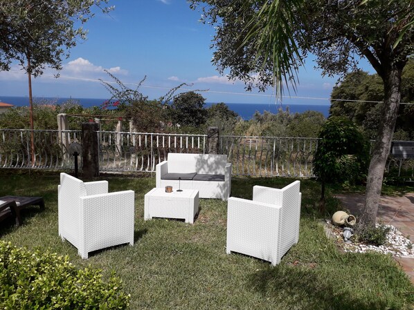 A patio with white wicker furniture, a small table, and a view of the sea. - Studio in villa with sea view (Tropea)
