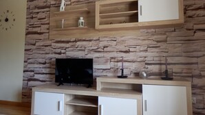 A living room with a stone wall, a flat-screen TV on a wooden stand, and built-in shelves with decorative items. - LOVE NEST IN CUENCA (Arcas)