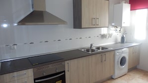 A modern kitchen with a built-in oven, a washing machine, and a stainless steel sink. - LOVE NEST IN CUENCA (Arcas)