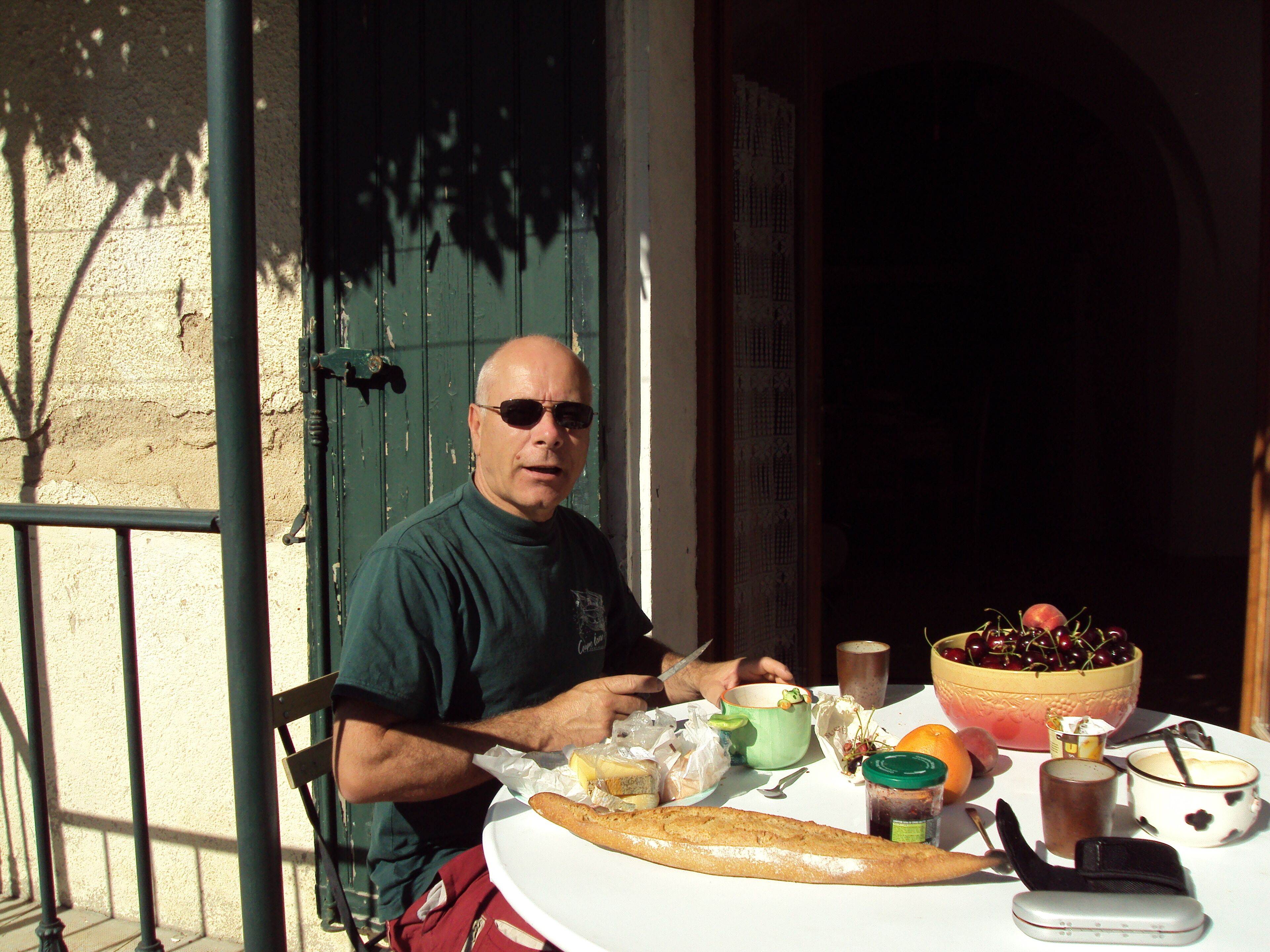 A man sitting at a table with food and drinks, a green door, and a balcony railing.