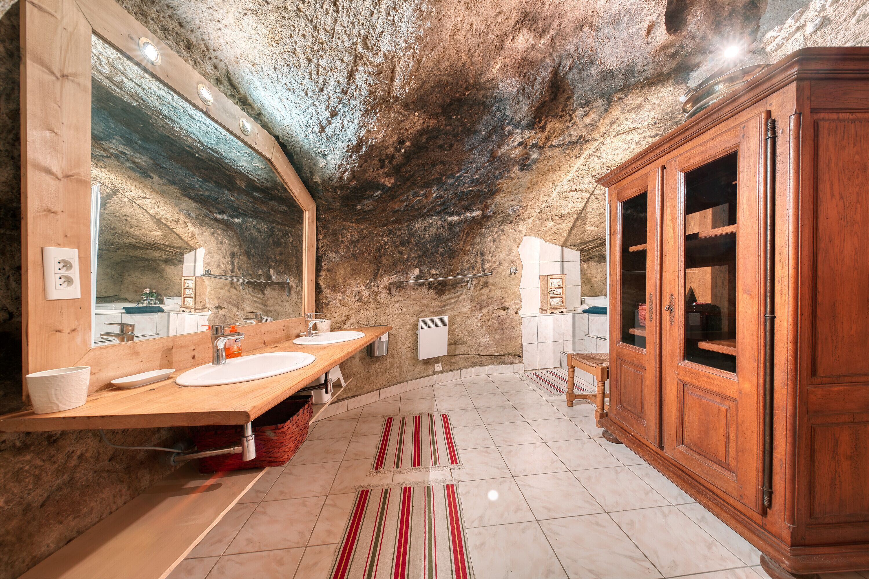 Une salle de bain rustique avec des meubles en bois, un grand miroir et un sol carrelé.