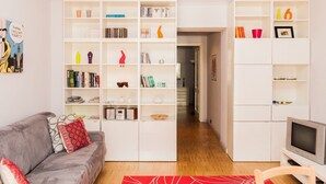 A modern living room with a grey sofa, white shelving units filled with books and decorative items, a flat-screen TV, and a red patterned rug. - Apartment/ flat -  city center - private parking included (Torino)