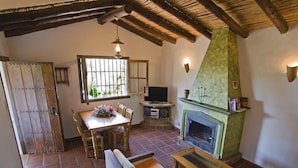 A cozy living room with a fireplace, wooden furniture, and a dining area with a window.