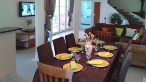 Un comedor con una larga mesa dispuesta para cuatro personas, rodeada de sillas. Hay un televisor montado en la pared a la izquierda.