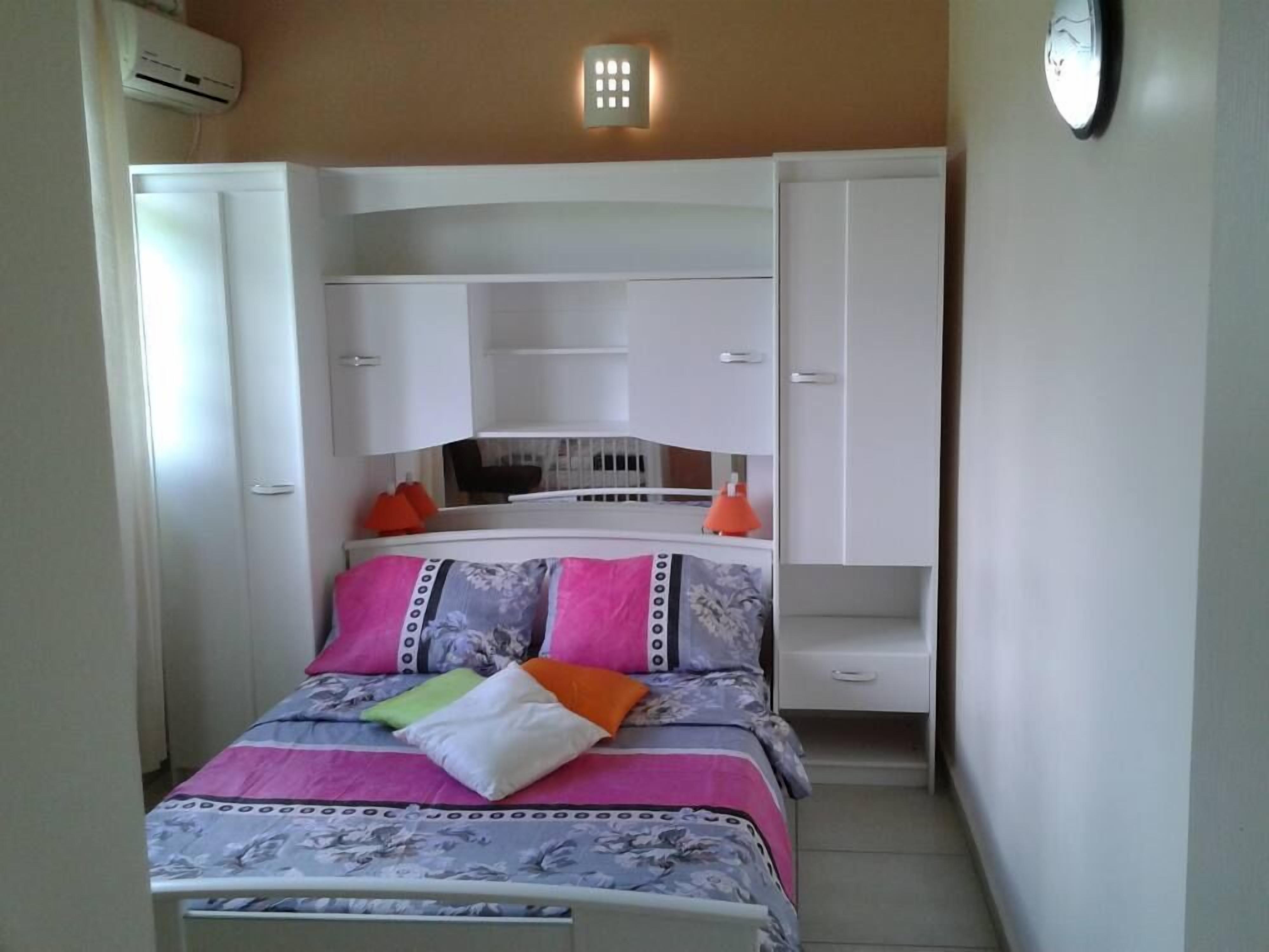 Een slaapkamer met een bed, een witte kledingkast en een klein bureau met een stoel.