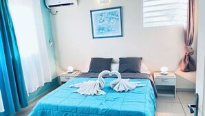 Habitación de hotel con cama, dos mesitas de noche, aire acondicionado de pared, un cuadro enmarcado y cortinas.