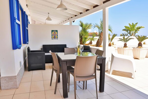 An outdoor patio with a dining table, chairs, and a sofa. There are potted plants and a view of the beach. - Typical house 200 meters from the sea wi fi car rental (balestrate)