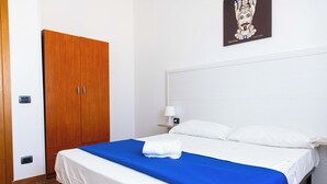 Une chambre à coucher comprenant un lit, une armoire en bois, une table de chevet avec une lampe et une œuvre d’art accrochée au mur.