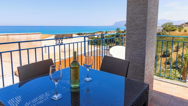 Une table avec une bouteille et deux verres sur un balcon donnant sur la mer.