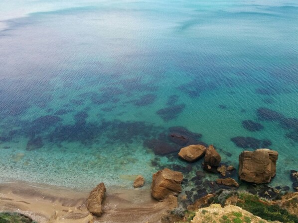 Enjoy the serene coastal landscape with turquoise waters and a sandy beach, surrounded by rugged rocks and a gentle slope.