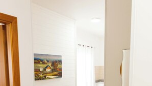 Un couloir avec une porte en bois, un tableau représentant un paysage rural et une salle de bain avec un rideau de douche.