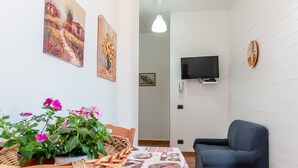 Une pièce chaleureuse avec un panier en osier rempli de fleurs, un canapé bleu, un téléviseur à écran plat et un téléphone fixé au mur.