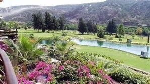 Une vue sur un terrain de golf avec un étang, entouré d’une végétation luxuriante et des montagnes en arrière-plan.