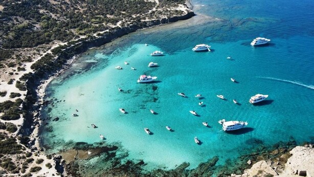 Une vue aérienne d’une zone côtière, avec des eaux turquoise limpides, de nombreux bateaux, ainsi qu’un mélange de plages de sable et de terrain rocheux.