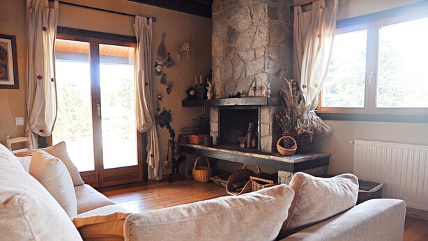 Ein gemütliches Wohnzimmer mit Kamin aus Stein, einer Couch und einem großen Fenster mit Vorhängen.