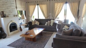 Een woonkamer met een bank, een salontafel, een open haard en een groot raam met gordijnen.
