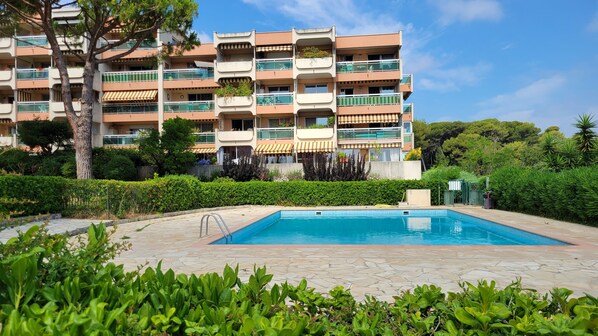 A multi-story residential building with balconies, a swimming pool, and surrounding greenery.
