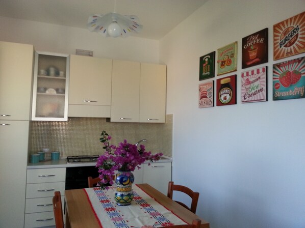 A kitchen with white cabinets, a tiled backsplash, and a dining table with a floral tablecloth. - apartment at 200 meters from the magnificent beach of Timpi Russi (sciacca)